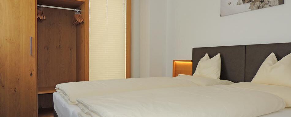A cozy bedroom with a large bed and two pillows. The wardrobe is open and the walls are light and plain. - Haus Christophorus - Obergurgl 