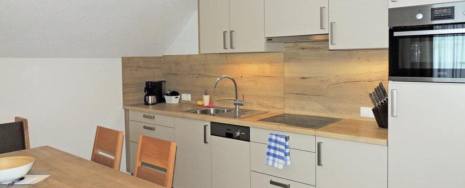A modern kitchen with a wooden stick and light-colored cabinets. Inside, there is a sink, a microwave, and a dining table with chairs. - Haus Christophorus - Obergurgl 
