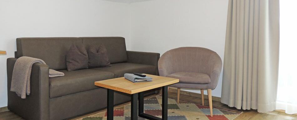 A cozy living room with a brown sofa and a beige armchair. The wooden table is on a colorful rug and the window lets in a lot of light. - Haus Christophorus - Obergurgl 