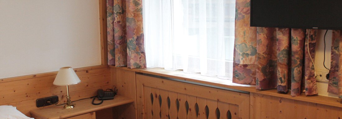 A cozy room with wooden paneling and a large window. A television, as well as a lamp and a telephone, are also present. - Haus Martinshof - Obergurgl 
