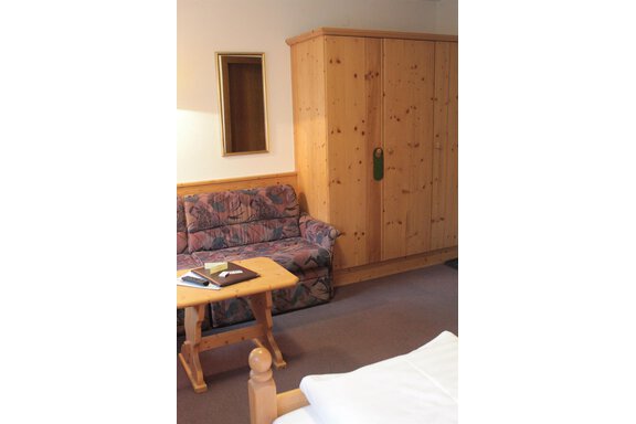 A cozy room with a sofa, a table, and a wooden cabinet. A small mirror hangs on the wall. - Haus Martinshof - Obergurgl 
