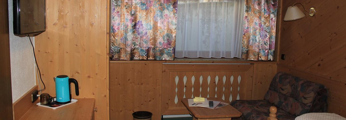A simple room with wooden furniture and a cozy design. There is a television, a table, and an armchair, as well as a desk. - Haus Martinshof - Obergurgl 