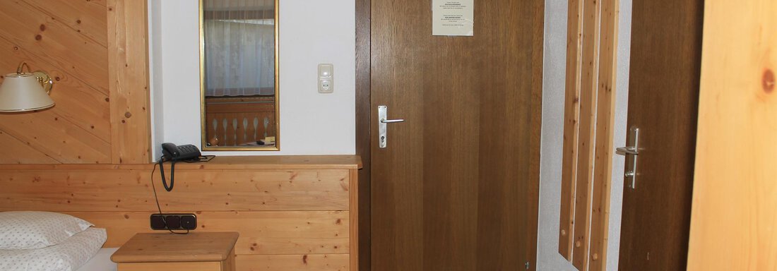 A simple room with wooden furniture and a double bed.  
On the wall, there is a mirror and the door leads outside. - Haus Martinshof - Obergurgl 