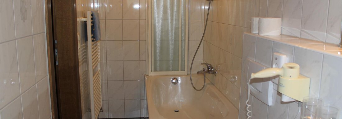 A small bathroom with a bathtub and a shower. The walls are tiled with white tiles and there is a towel holder. - Haus Martinshof - Obergurgl 