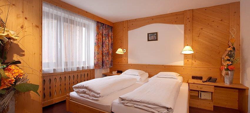 A cozy room with two single beds and warm wooden furniture. Large windows provide plenty of daylight. - Haus Martinshof - Obergurgl 