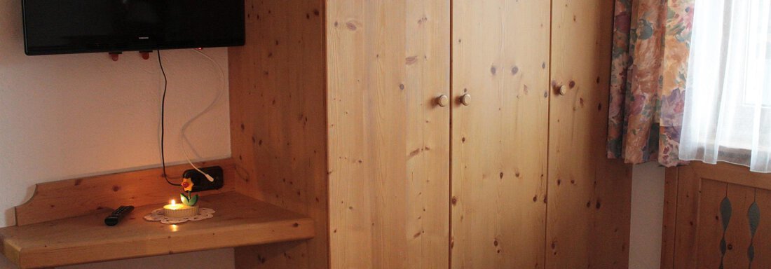 A cozy room with a large wooden cabinet and a television on the wall. A small light source is on the table, and there is bright bed linen. - Haus Martinshof - Obergurgl 