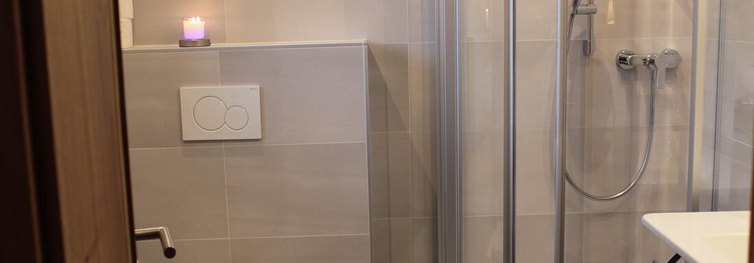A modern bathroom with a shower and a toilet. The walls are brightly tiled, and a candle provides a cozy atmosphere. - Haus Martinshof - Obergurgl 