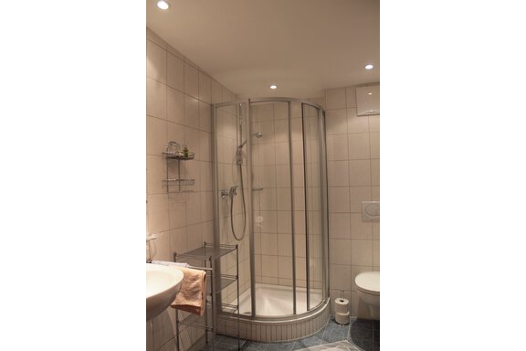 A modern bathroom with a glass shower and white tiles. There is a sink and a toilet in the corner. - Haus Martinshof - Obergurgl 