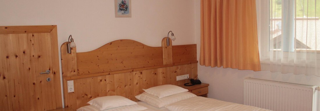 A cozy bedroom with two single beds and wood-paneled walls. The room has large windows with curtains and a warm atmosphere. - Haus Martinshof - Obergurgl 