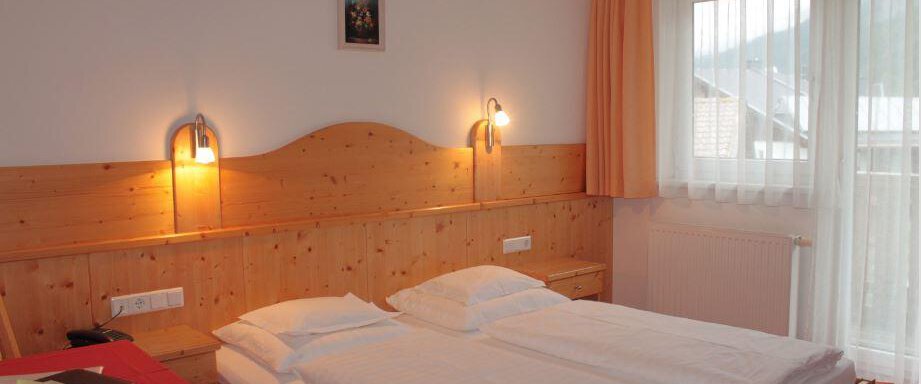 A cozy room with a wooden double bed. The walls are painted light, and large windows provide plenty of daylight. - Haus Martinshof - Obergurgl 
