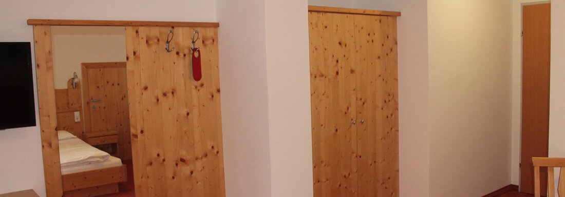 A cozy room with wooden furniture and carpeted floor. There is a television and a box of shoes. - Haus Martinshof - Obergurgl 
