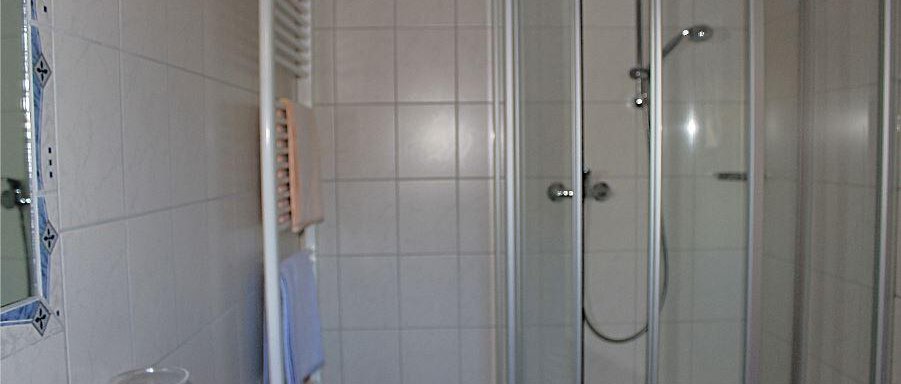 A modern bathroom with a shower and white tiles. Towels hang on a towel radiator. - Haus Martinshof - Obergurgl 