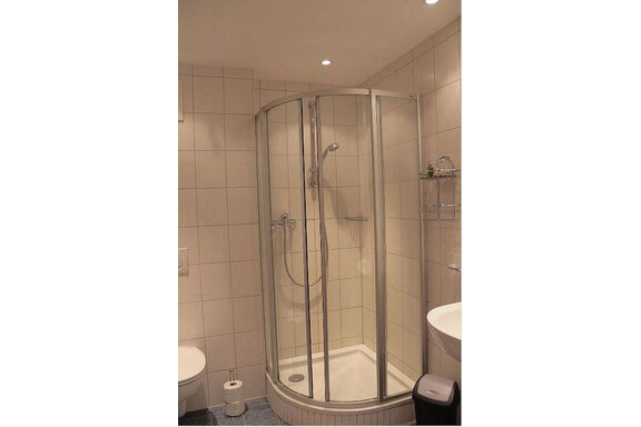 A modern bathroom with a glass shower cabin. The walls are tiled with light tiles and there is a toilet as well as a sink. - Haus Martinshof - Obergurgl 