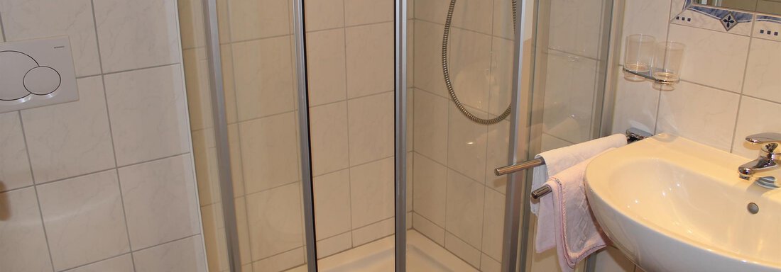A modern bathroom with a shower cabin, a sink, and a toilet. The walls are tiled and the furnishings are simple and functional. - Haus Martinshof - Obergurgl 