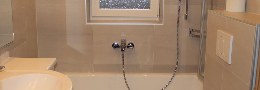 A modern bathroom with a bathtub and a shower. There is a sink and a window that lets in natural light. - Haus Martinshof - Obergurgl 