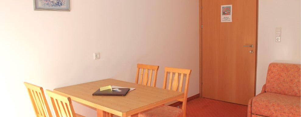 A bright room with a table and chairs, as well as a sofa. A picture hangs on the wall and the door is closed. - Haus Martinshof - Obergurgl 
