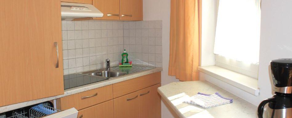 A bright kitchen with wooden cabinets and a large window. On the countertop, there is a coffee machine and some utensils. - Haus Martinshof - Obergurgl 