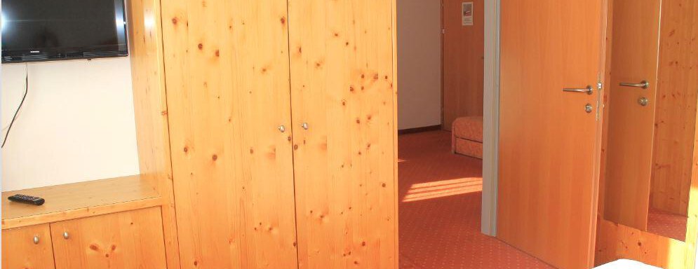 A simply furnished room with wooden cabinets and a television on the wall. The doors lead to another room. - Haus Martinshof - Obergurgl 