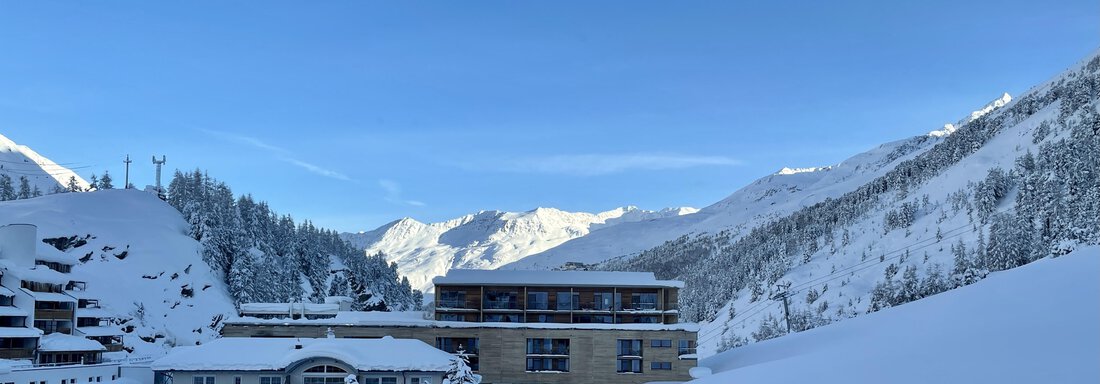A snow-covered mountain landscape with a modern building in the foreground. The clear blue sky complements the wintry scenery. - Haus Verwall Appartements - Obergurgl 