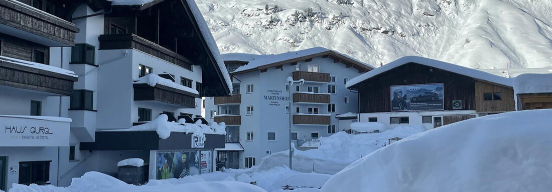 A snowy landscape with modern chalets and high mountains in the background. The buildings are covered by a thick layer of snow. - Haus Verwall Appartements - Obergurgl 