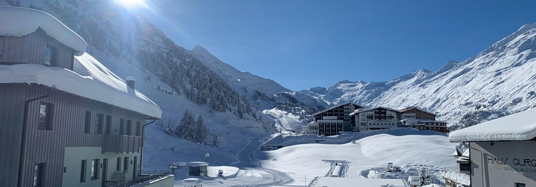 A snowy landscape with mountains and a clear blue sky. In the foreground, modern buildings can be seen. - Haus Verwall Appartements - Obergurgl 