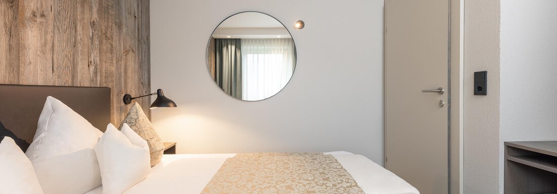 A modern bedroom with a large bed and elegant pillows. A round mirror and a stylish wall complement the cozy atmosphere. - Haus Verwall Appartements - Obergurgl 
