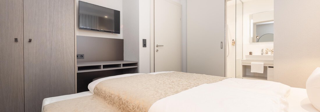 A modern hotel room with two beds and a television. In the background, the bathroom is visible. - Haus Verwall Appartements - Obergurgl 