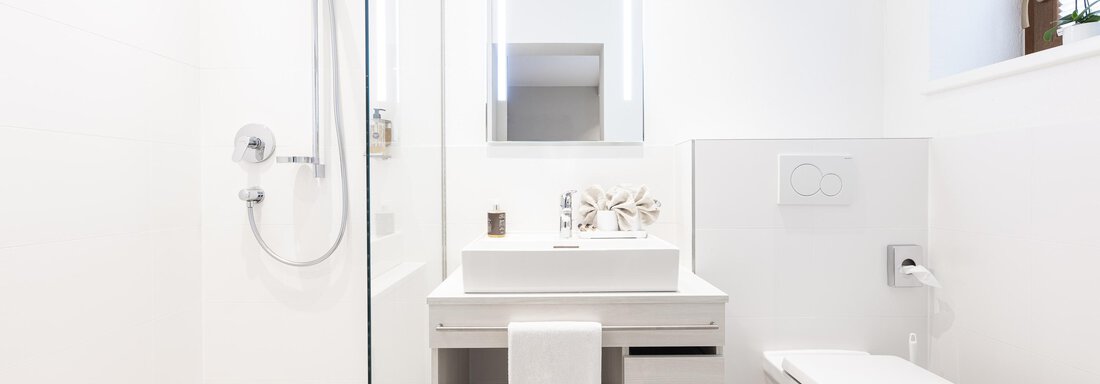 A modern bathroom with a shower and a sink. The walls and furniture are in bright white. - Haus Verwall Appartements - Obergurgl 