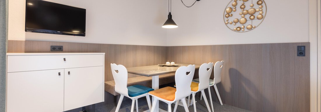 A modern dining area with a table and six colorful chairs. A television and decorative wall art hang on the wall. - Haus Verwall Appartements - Obergurgl 