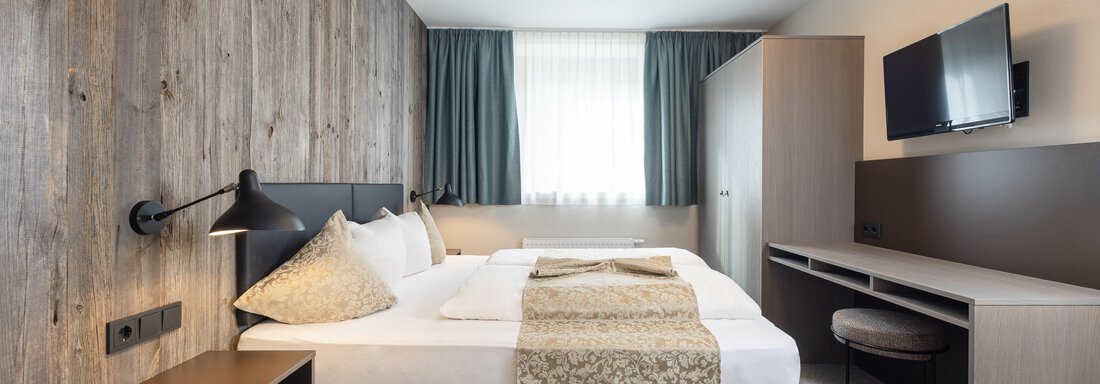 A modern bedroom with a double bed and wooden walls. There is a desk and a television on the wall. - Haus Verwall Appartements - Obergurgl 