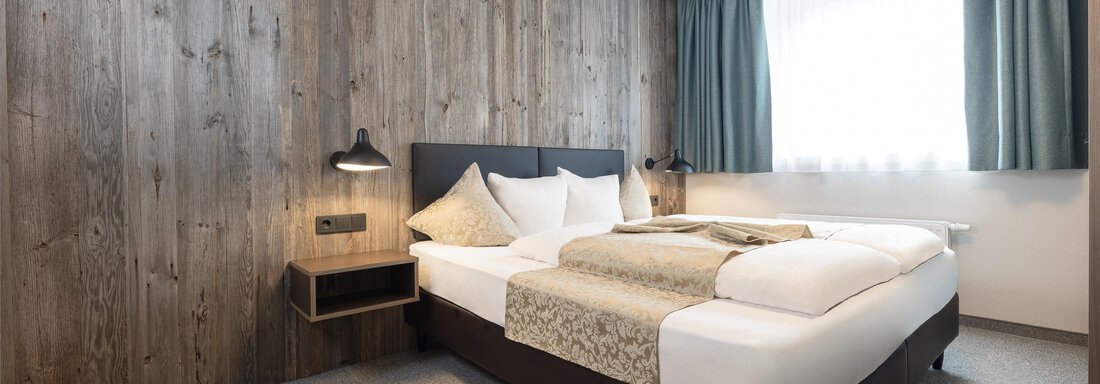 A modern bedroom with a large double bed. The walls are made of wood and the windows are decorated with green curtains. - Haus Verwall Appartements - Obergurgl 