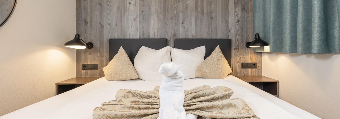 A cozy bedroom with a large bed and decorative pillows. An artfully folded towel figure sits on the bedspread. - Haus Verwall Appartements - Obergurgl 