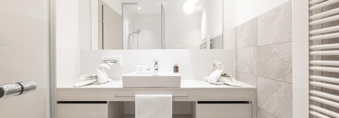 A modern bathroom with a bright vanity and a large mirror. The walls are in neutral tones, and there are towels as well as pleasant lighting. - Haus Verwall Appartements - Obergurgl 