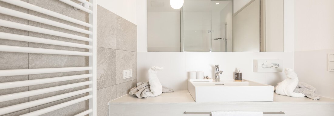 A modern bathroom with a large mirror and an elegant sink. Towels and a radiator are also visible. - Haus Verwall Appartements - Obergurgl 
