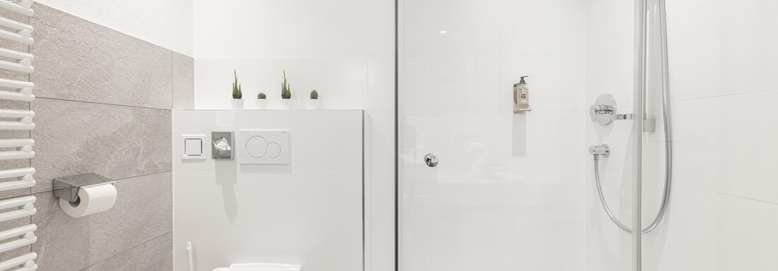 A modern bathroom with a shower and a toilet. The walls are bright and designed in a minimalist style. - Haus Verwall Appartements - Obergurgl 