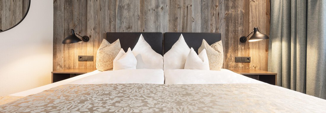 A modern bedroom with a large bed and stylish pillows. The walls are made of wood and there are decorative lamps. - Haus Verwall Appartements - Obergurgl 