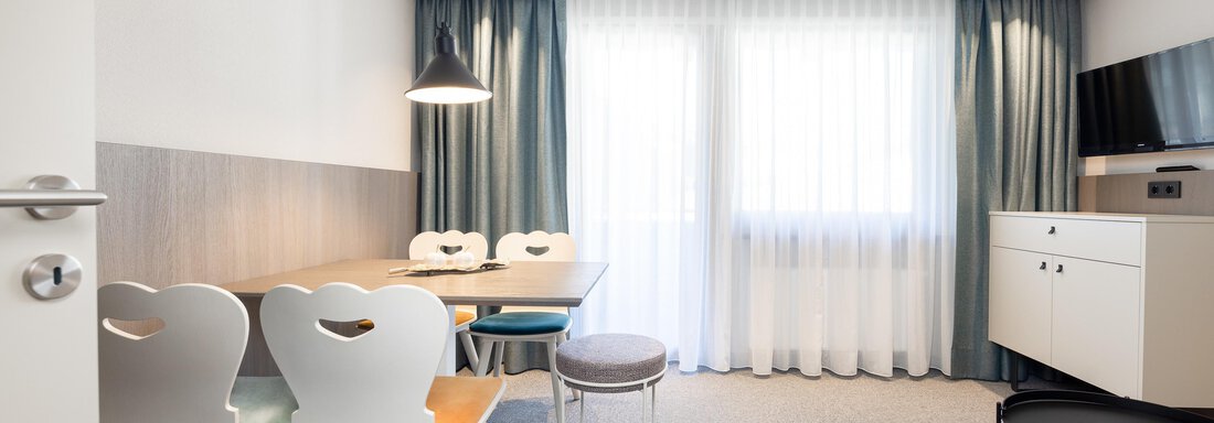 A modern living room with a dining area and large windows that let in plenty of daylight. The furniture is simple and stylish, with a neutral color palette. - Haus Verwall Appartements - Obergurgl 