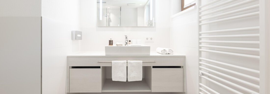 A modern bathroom with a white sink and large mirror. The space is bright and designed minimally. - Haus Verwall Appartements - Obergurgl 