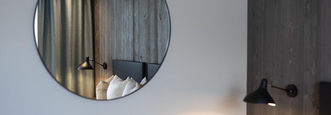 A modern room with a round mirror. In the background, curtains and a bedside lamp can be seen. - Haus Verwall Appartements - Obergurgl 