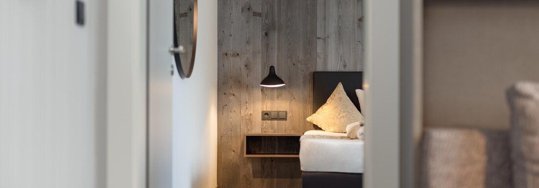 A modern bedroom with a cozy bed and a wooden panel on the wall.  
Comfortable furniture and soft lighting create a relaxed atmosphere. - Haus Verwall Appartements - Obergurgl 