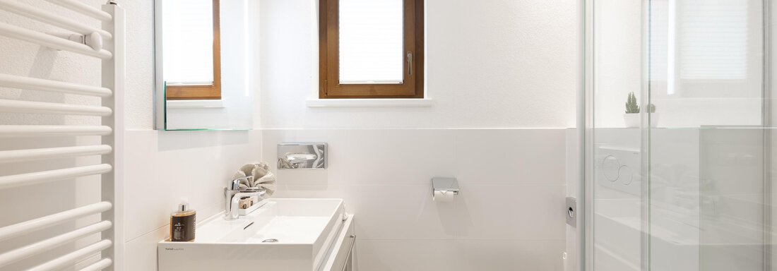 A modern bathroom with a bright design. It features a sink, a shower, and a window. - Haus Verwall Appartements - Obergurgl 