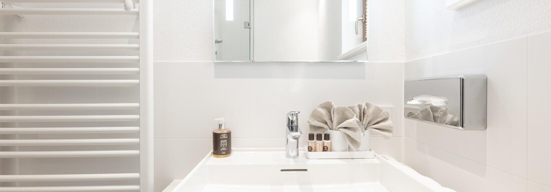 A modern bathroom with a white sink and large mirror. The room has bright walls and a metal towel holder. - Haus Verwall Appartements - Obergurgl 