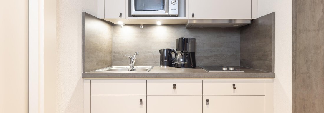 A modern mini kitchen with white cabinets and a microwave. The amenities include a sink and a coffee maker. - Haus Verwall Appartements - Obergurgl 