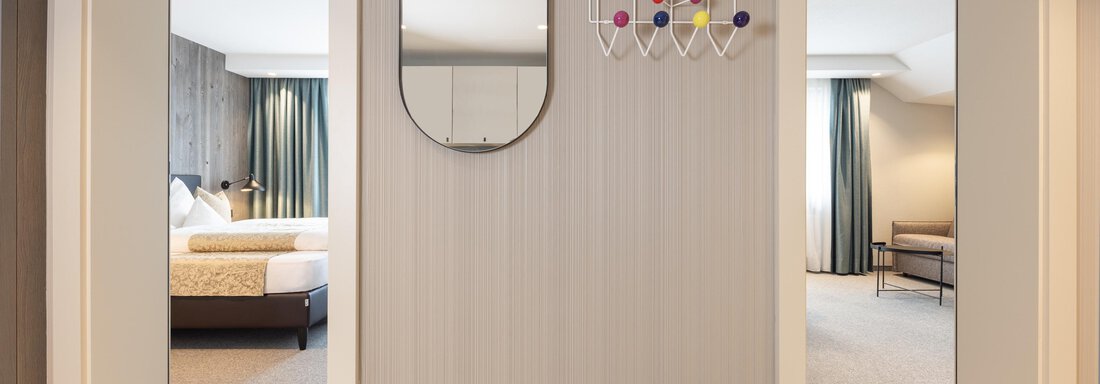 A modern hallway with two open doors to hotel rooms. A round mirror and a colorful wall decoration hang on the wall. - Haus Verwall Appartements - Obergurgl 