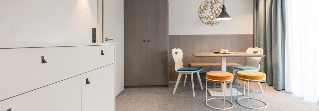A modern living room with a dining area. There are bright furniture and large windows that let in a lot of light. - Haus Verwall Appartements - Obergurgl 