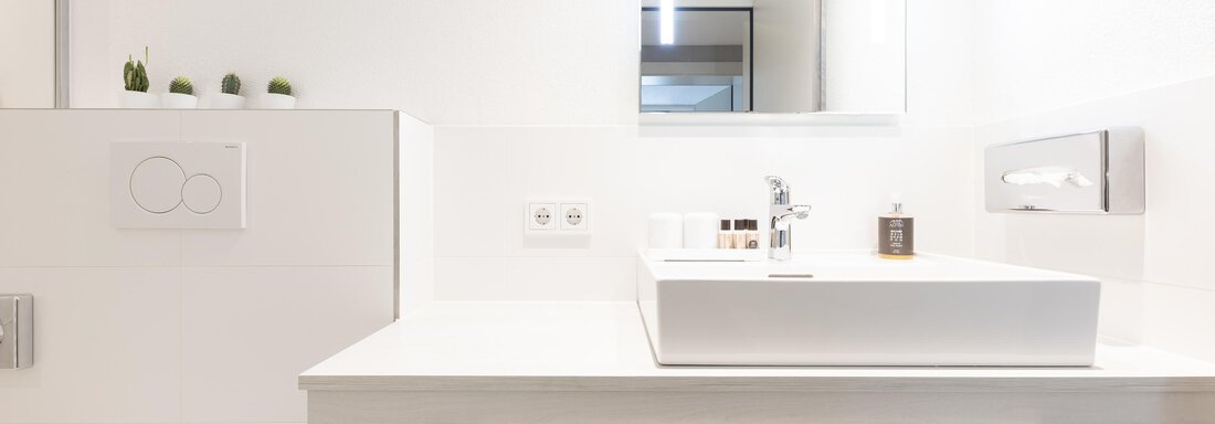 A modern bathroom with a simple white sink and a large mirror. Bright walls and a minimalist decor create an inviting atmosphere. - Haus Verwall Appartements - Obergurgl 