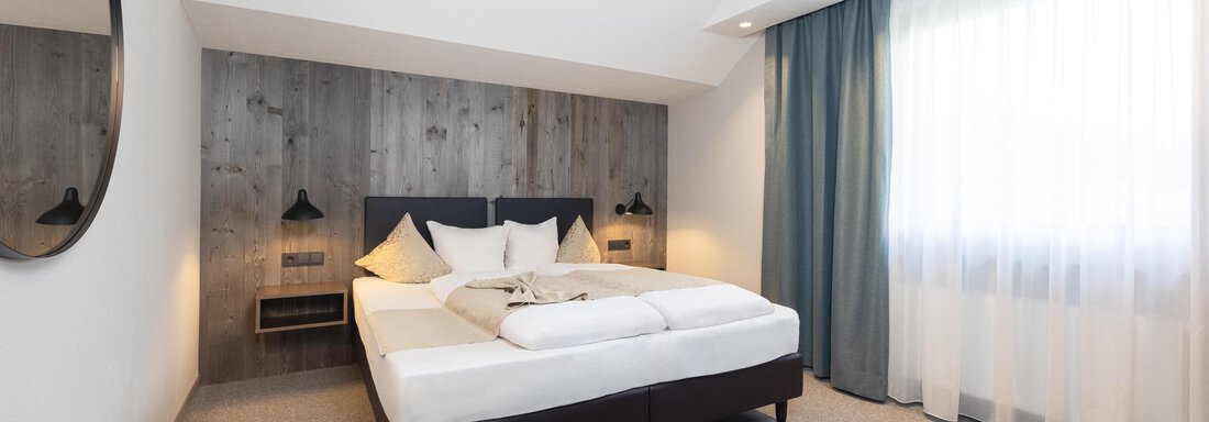 A modern bedroom with a large double bed and bright, inviting light. The walls are painted in neutral colors and there is a round mirror. - Haus Verwall Appartements - Obergurgl 