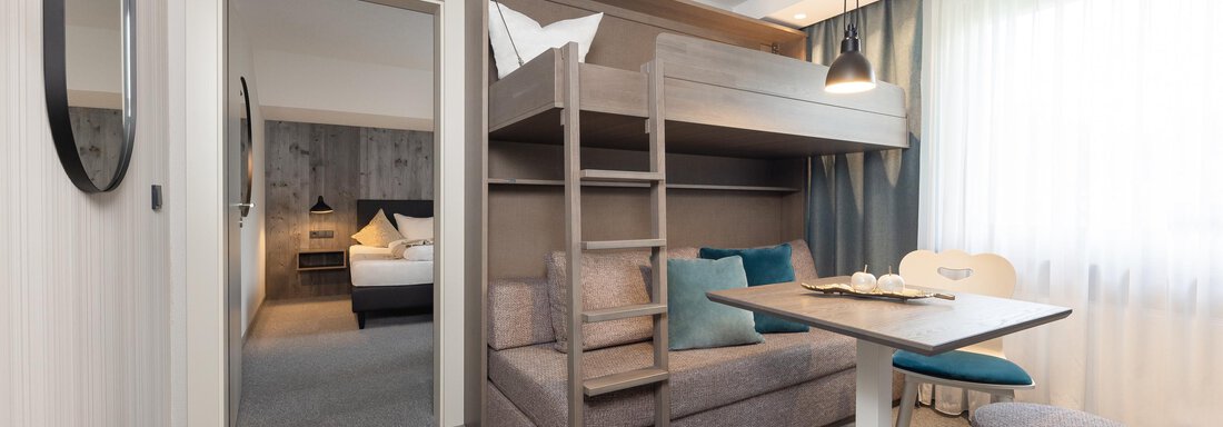 A modern room with a loft bed and a cozy seating area. The large window front allows plenty of daylight in. - Haus Verwall Appartements - Obergurgl 