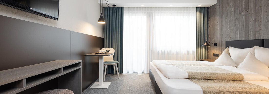 A modernly furnished hotel room with two beds and a desk. Large windows let in plenty of daylight. - Haus Verwall Appartements - Obergurgl 