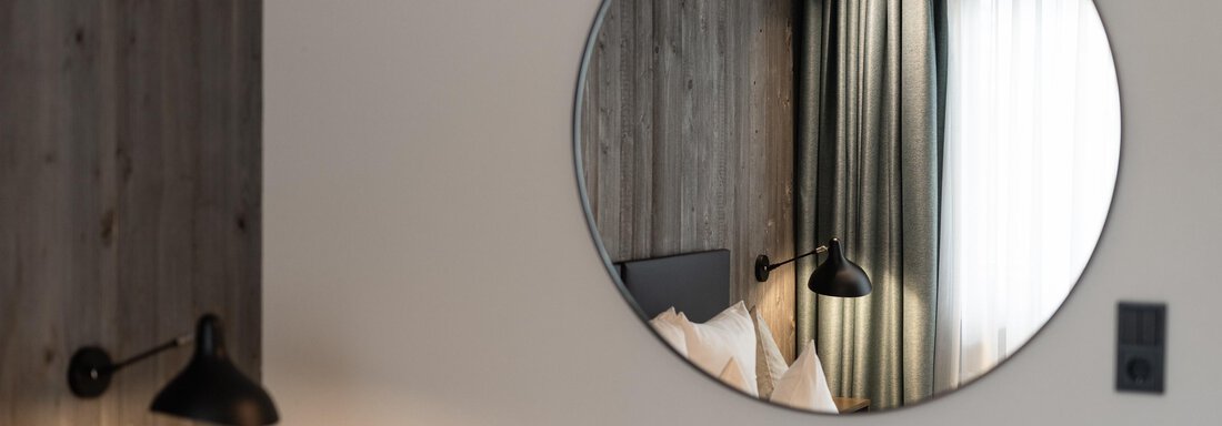 A modern room with a round mirror on the wall. In the background, curtains and a bed are visible. - Haus Verwall Appartements - Obergurgl 